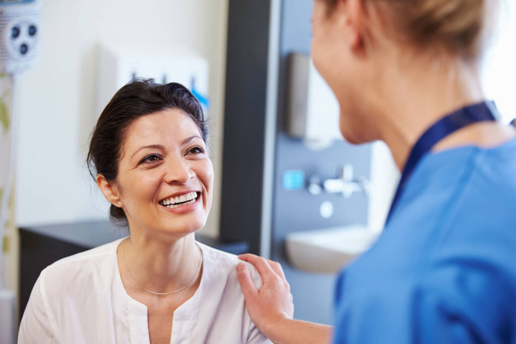 a woman smiling talking to her doctor. the doctor has a hand over her shoulder smiling back