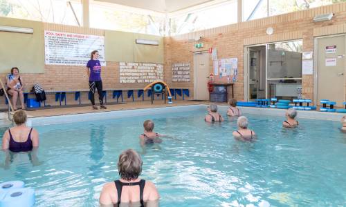 A group of people exercising in a pool doing hydrotherapy following instructor. Photo taken at Arthritis & Osteoporosis premises.