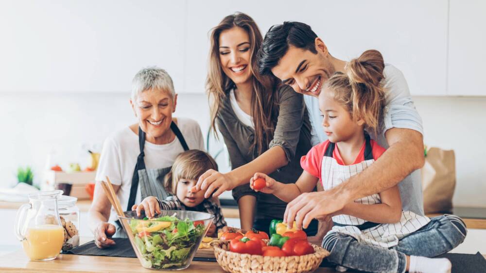A family making a salad. Grandmother, mother, father, daughter in the counter top, and son helping with the meal.