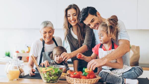 A family making a salad. Grandmother, mother, father, daughter in the counter top, and son helping with the meal.
